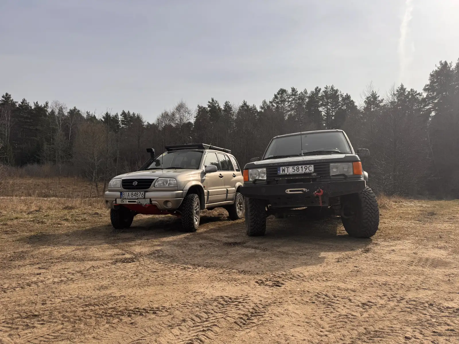 Suzuki Grand Vitara i Range Rover na piaszczystym placu pod lasem